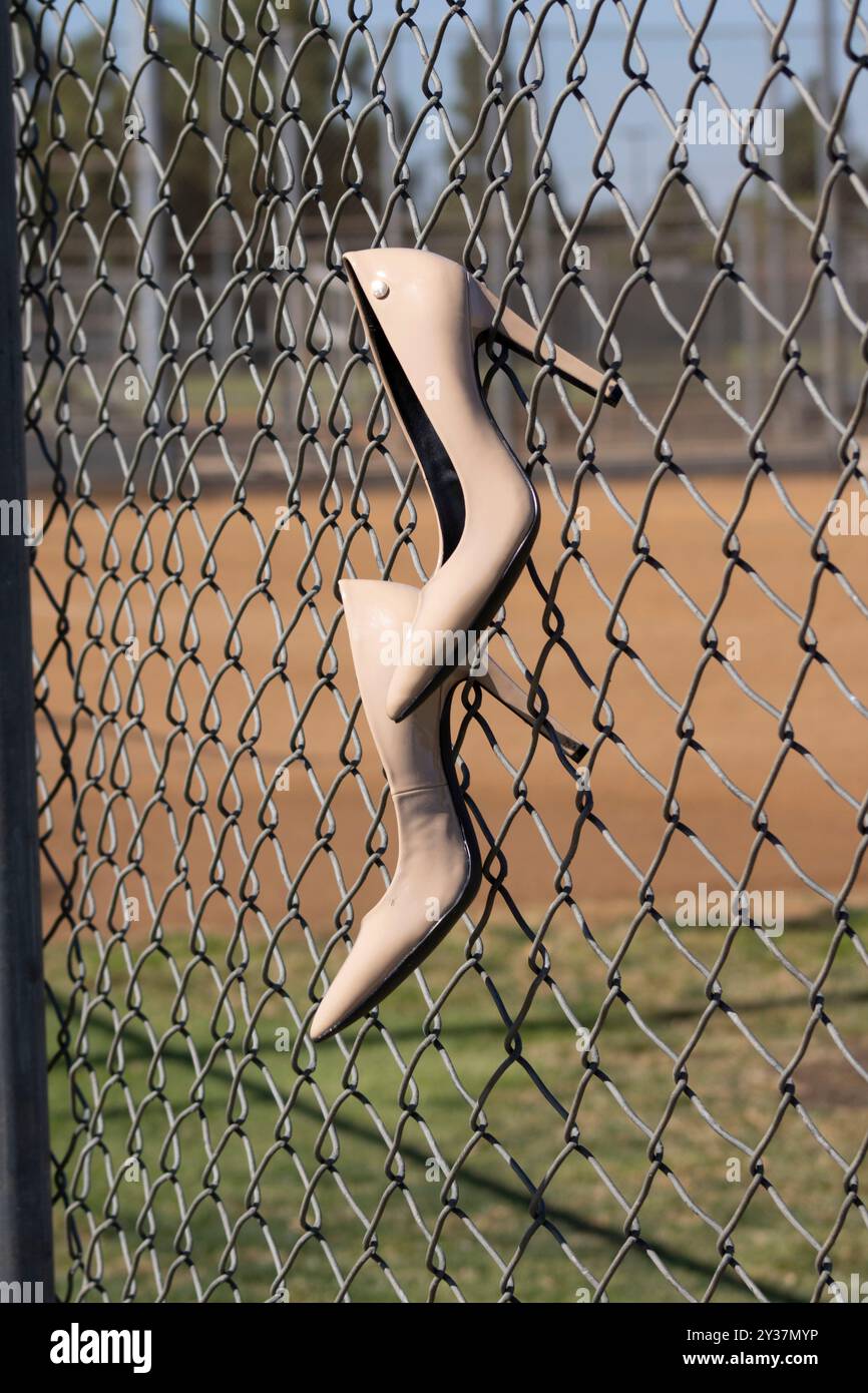 Beige Schuhe mit hohem Absatz, die am Kettenzaun des Baseballfeldes hängen Stockfoto