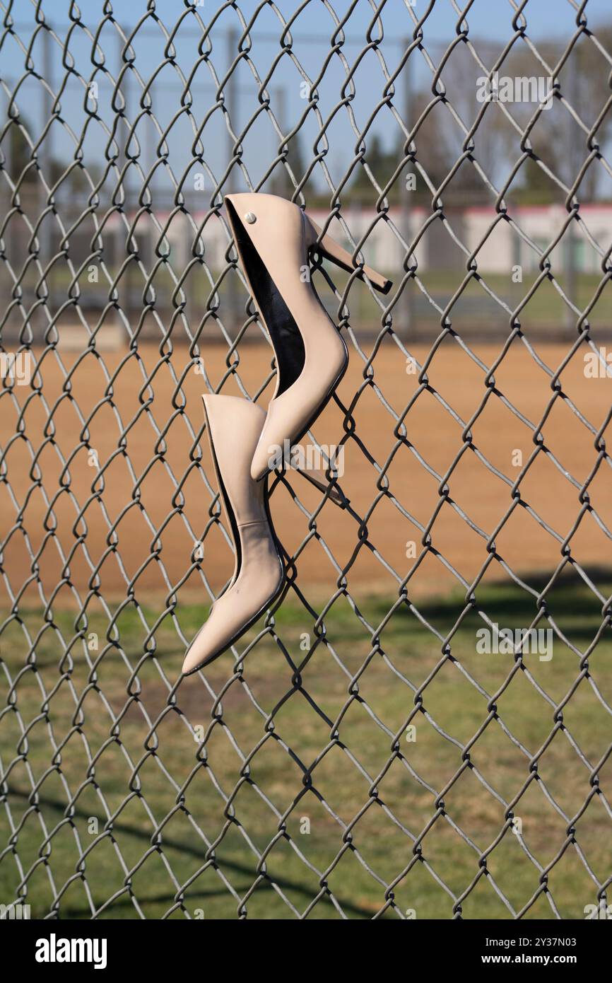 Beige Schuhe mit hohem Absatz, die am Kettenzaun des Baseballfeldes hängen Stockfoto