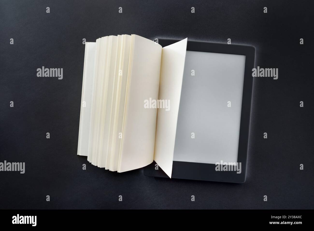 Digitales Lesekonzept mit E-Book auf schwarzem Tisch und Papierblättern, die sich aus dem Gerät ausklappen. Draufsicht Stockfoto