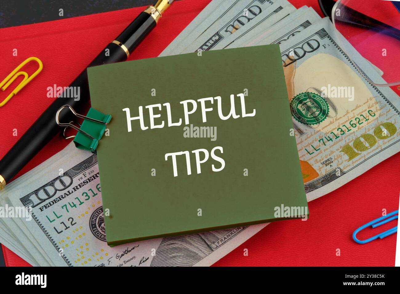 Hilfreiche Tipps Wörter auf einem grünen Aufkleber auf dem Hintergrund von Dollarscheine auf dem roten Buch Stockfoto