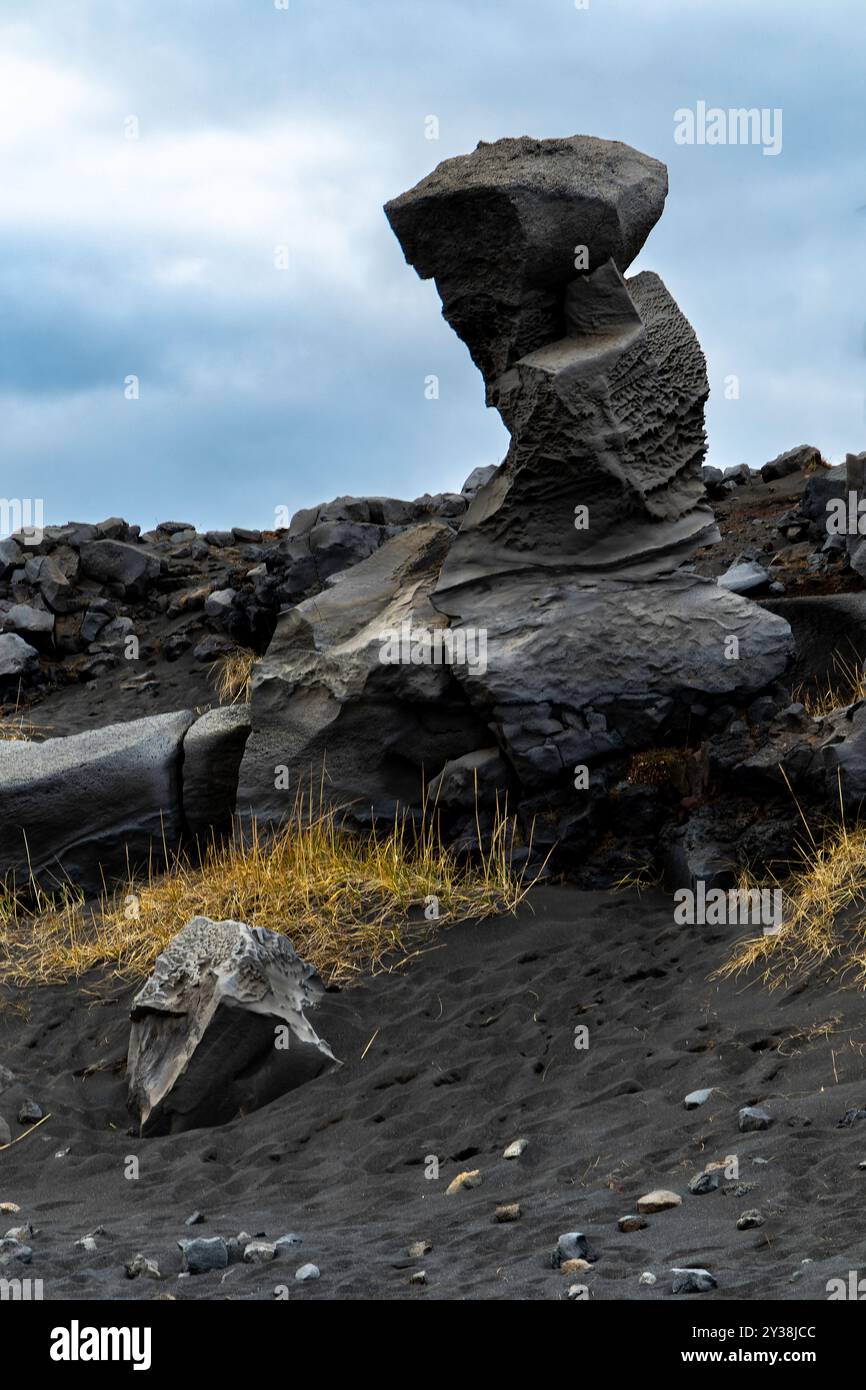 Ein großer Felsen liegt auf einem felsigen Hügel. Vulkanisches Gelände. Der Himmel ist bewölkt und der Felsen ist von einem Grasfeld umgeben Stockfoto