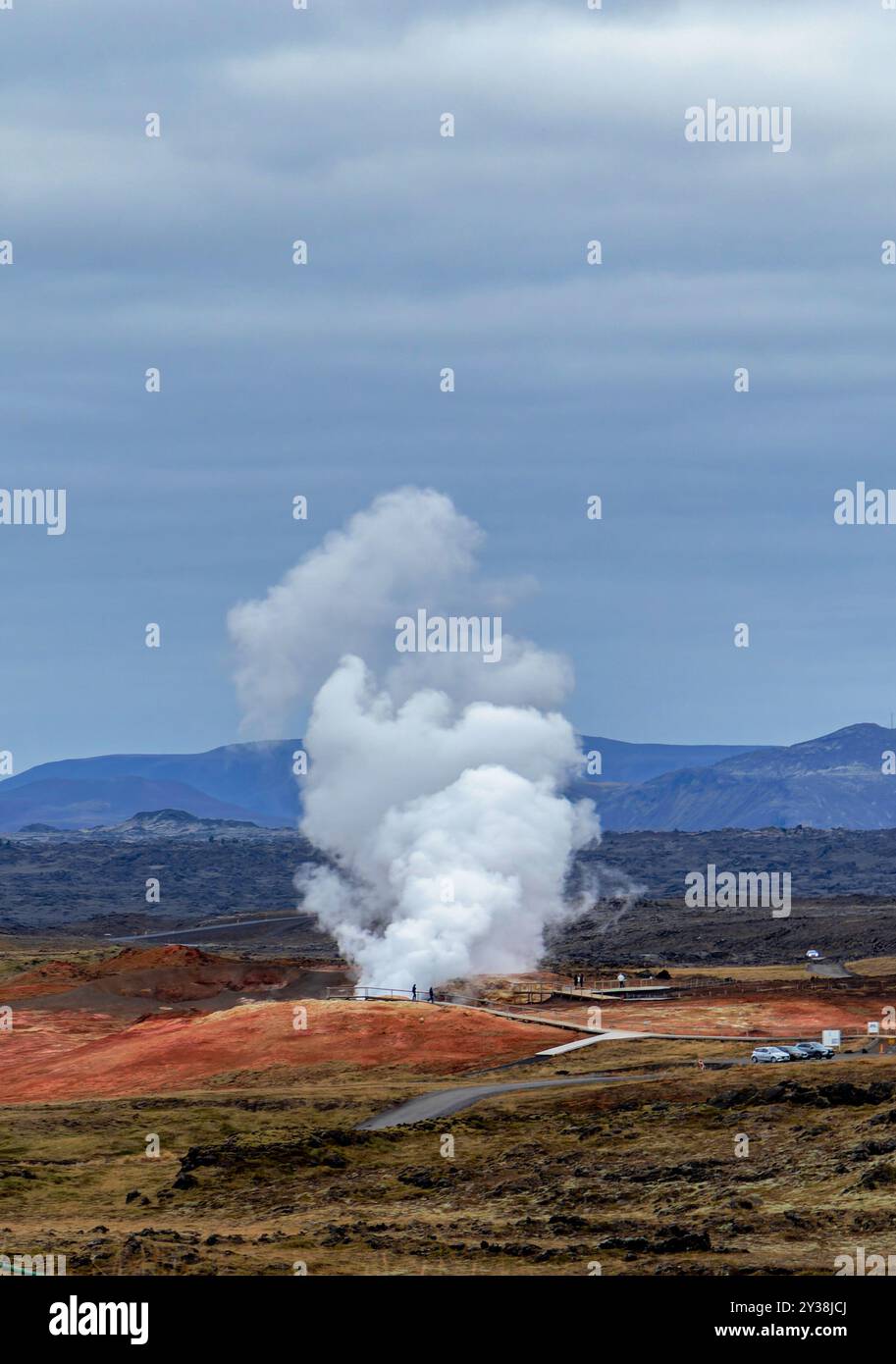 Eine große Dampfwolke steigt aus einem geothermischen Kraftwerk in der Ferne auf. Der Himmel ist bewölkt und die Landschaft unfruchtbar. Kraftwerk Reykjanes Stockfoto