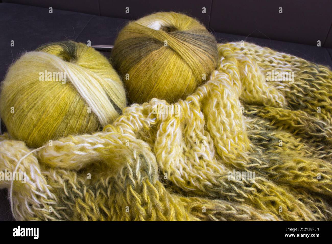 Verlaufsfarbene Garnkugel mit Strickjacke und Stricknadeln. Zitronenfarbene Alpaka- und Wollfäden mit wunderschönem Strickmuster. Stockfoto
