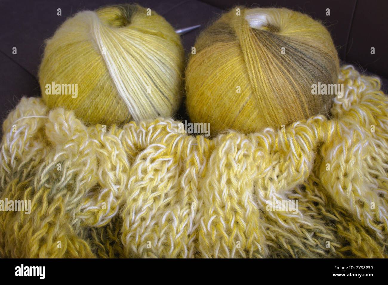 Verlaufsfarbene Garnkugel mit Strickjacke und Stricknadeln. Zitronenfarbene Alpaka- und Wollfäden mit wunderschönem Strickmuster. Stockfoto