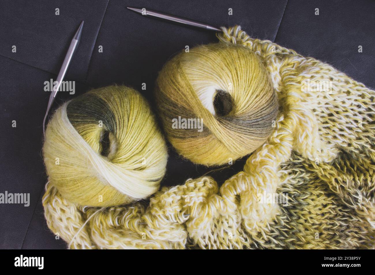 Verlaufsfarbene Garnkugel mit Strickjacke und Stricknadeln. Zitronenfarbene Alpaka- und Wollfäden mit wunderschönem Strickmuster. Stockfoto