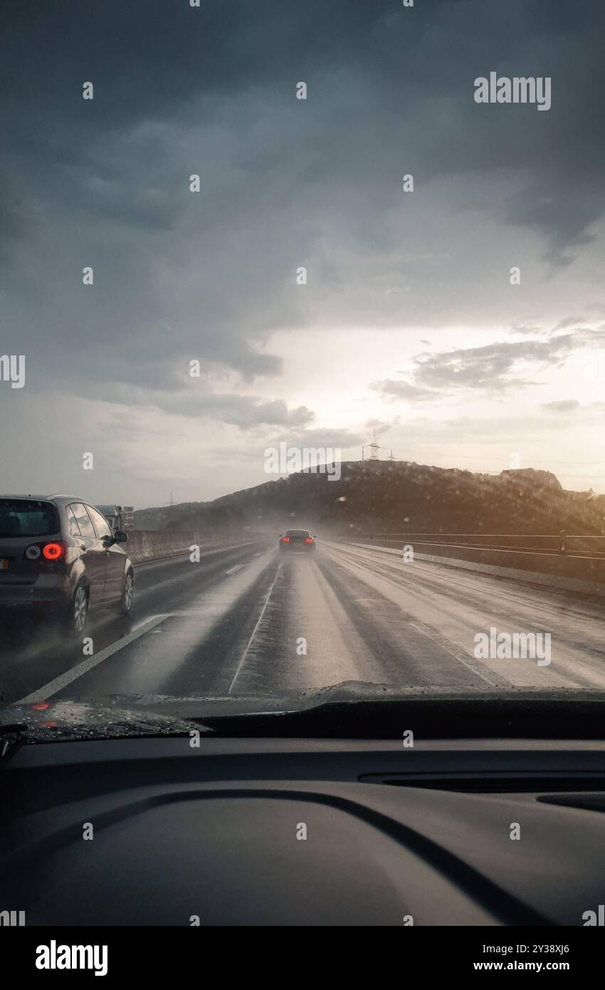 Bei Regen auf der Autobahn fahren. Schwindender perspektivischer Blick auf das Autofahren auf der deutschen Autobahn bei Sonnenuntergang. Stockfoto