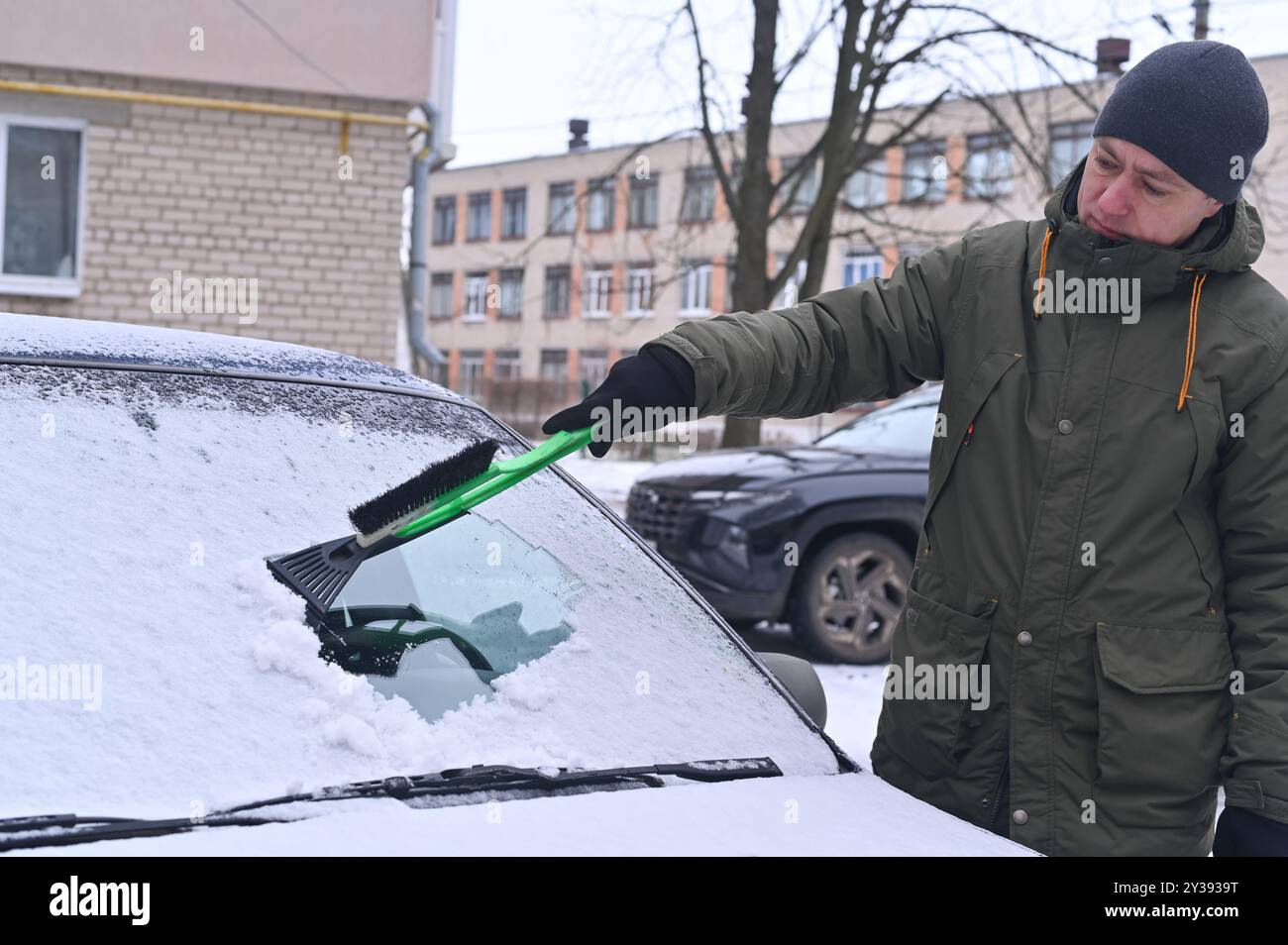 Ein Mann reinigt den festsitzenden Schnee von den Fenstern eines Autos Stockfoto