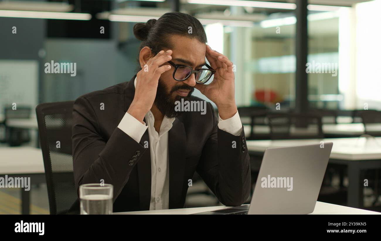 Gestresster kranker indischer männlicher Arbeitgeber Unternehmen arabischer Unternehmer Boss CEO Geschäftsmann muslimischer Geschäftsmann im Büro mit Laptop arbeitet Stockfoto
