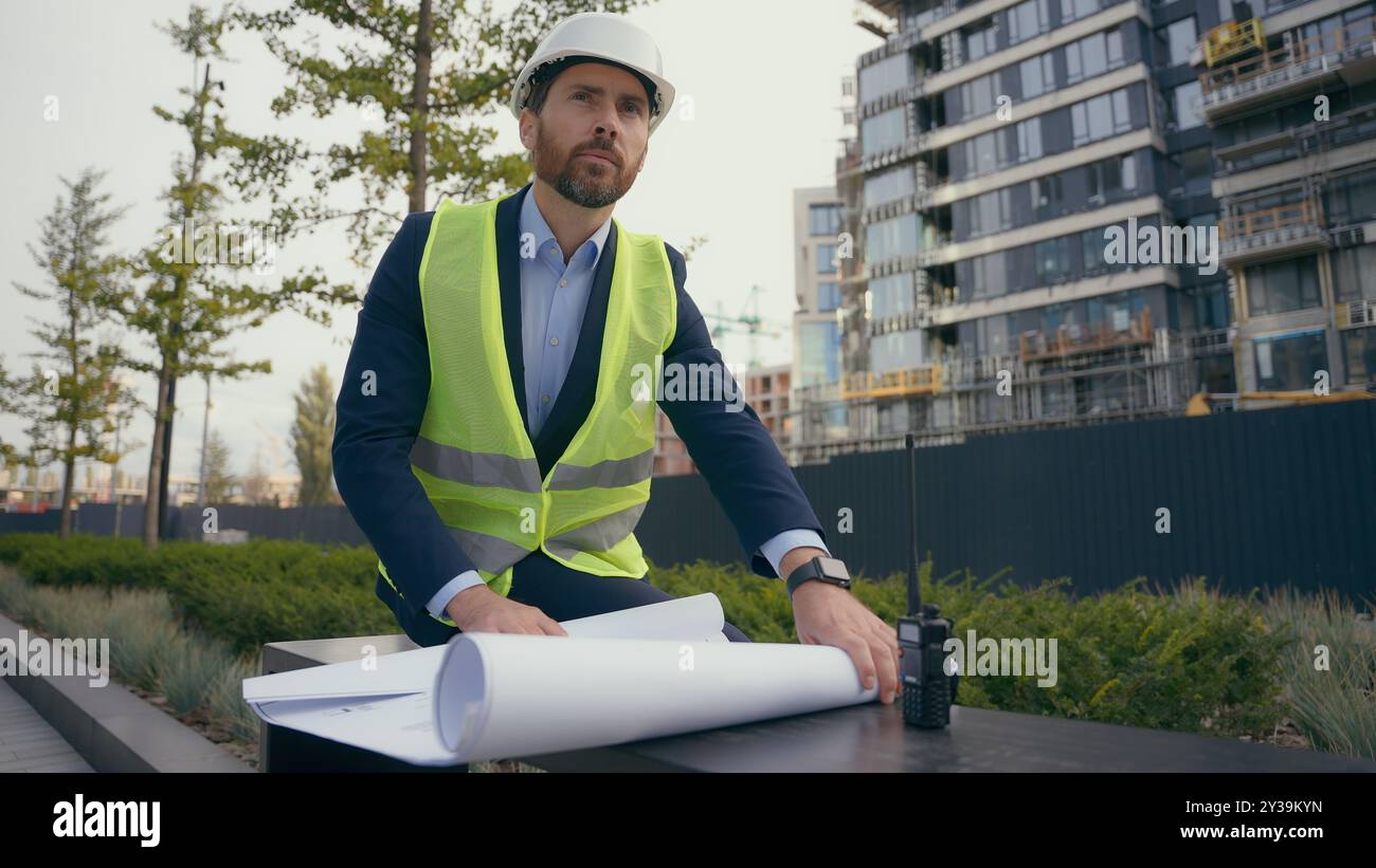 Kaukasischer lächelnder erwachsener Mann in der Stadt mit Blueprint Papier Dokument Plan Arbeit im Freien männlicher Architekt Guy prüft städtische Gebäude Architektur Geschäft Stockfoto