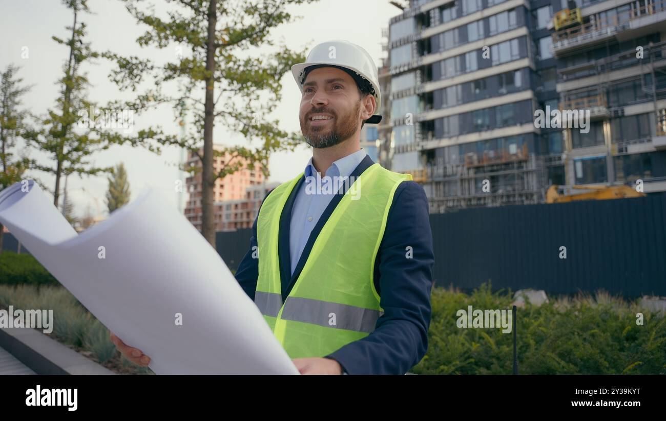 Kaukasischer lächelnder erwachsener Mann in der Stadt mit Blueprint Papier Dokument Plan Arbeit im Freien männlicher Architekt Guy prüft städtische Gebäude Architektur Geschäft Stockfoto
