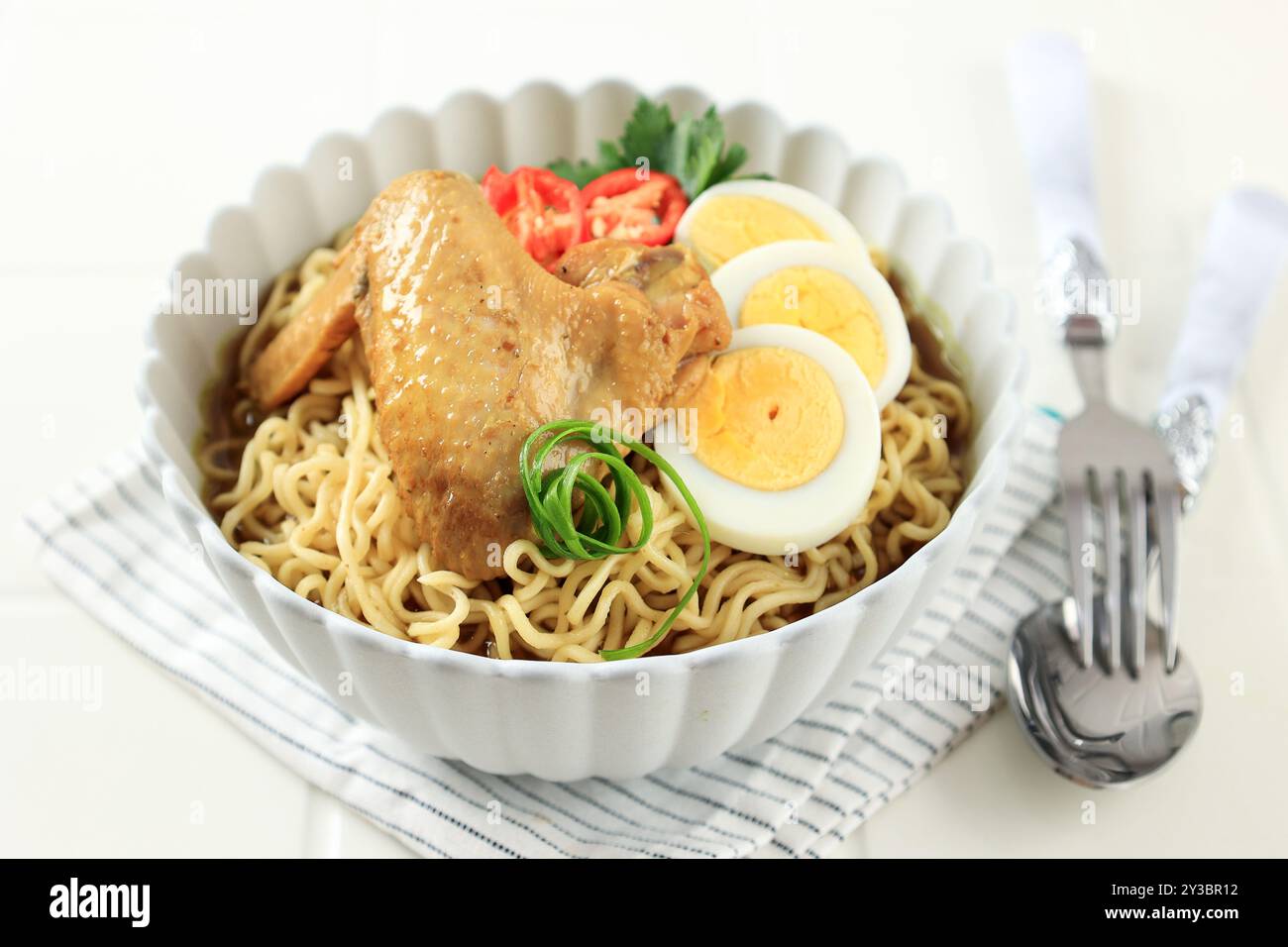 Indomie Rebus oder Instant Boiled Nudeln mit Soto-Geschmack, indonesische Instant Nudeln mit geschnittenem gekochtem Ei, Tomaten und Hühnerflügel Stockfoto