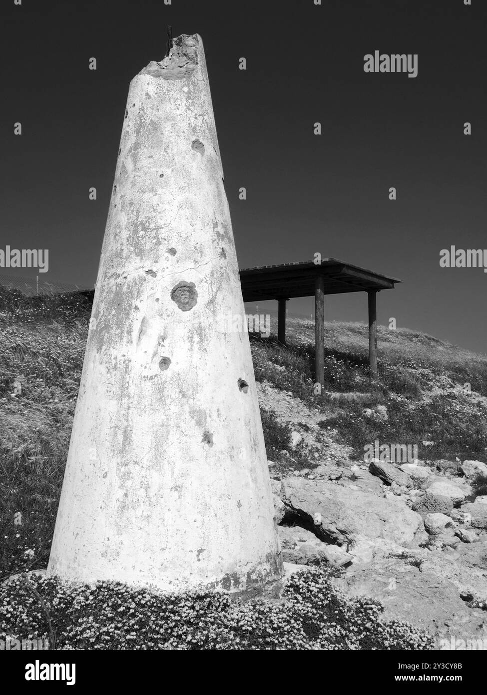 Ein gebrochenes weißes konisches Betonwerk neben einem Unterschlupf an den Küstenklippen, umgeben von Frühlingsblumen in paphos zypern Stockfoto