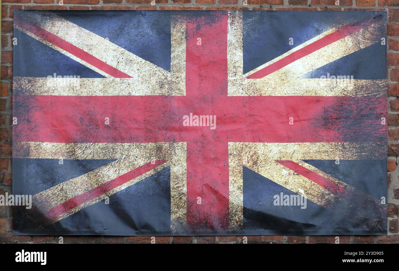 Eine alte, schmutzige britische Flagge mit dunklen zerknitterten Kanten auf einem Backsteinmauerhintergrund Stockfoto