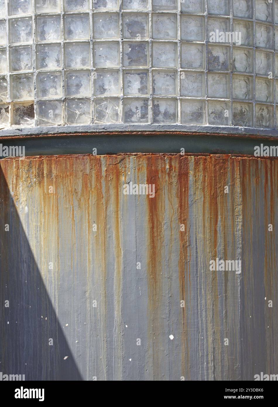 Eine gekrümmte graue Betonwand mit Reihen von quadratischen Fenstern oben, die mit Rost überzogen sind Stockfoto