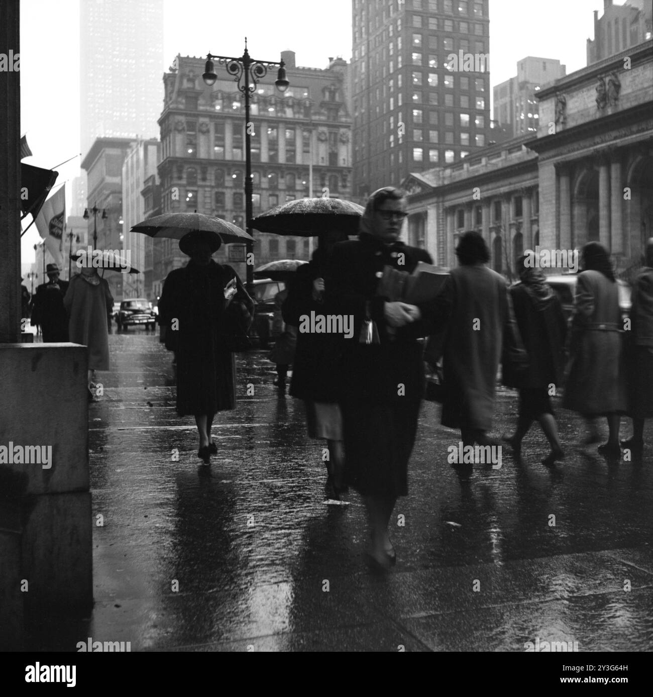 Fußgänger laufen auf der regnerischen 5th Avenue in New York City nahe der Kreuzung der 42nd Street und der New York Public Library. Stockfoto