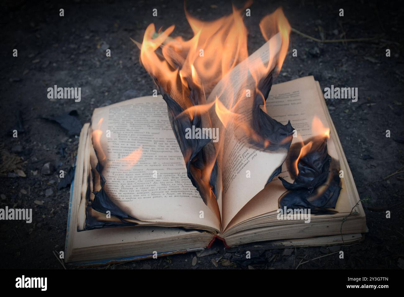 Das Foto zeigt ein hell brennendes Buch, dessen Seiten im Wind flattern und Flammen den umgebenden Raum erleuchten. Das Feuer scheint seine zu manifestieren Stockfoto