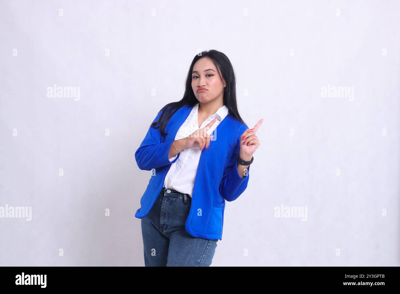 Der Charme einer schönen jungen indonesischen Bürofrau, die einen blauen formalen Anzug trägt und die Stirn runzelnd mit beiden Händen nach oben links zeigt. Für Corpo Stockfoto