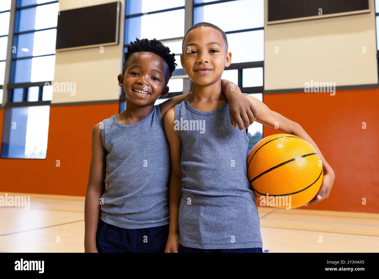 Im Fitnessstudio der Schule lächeln zwei multirassische Jungen und halten Basketball, um sportliche Aktivitäten zu genießen Stockfoto
