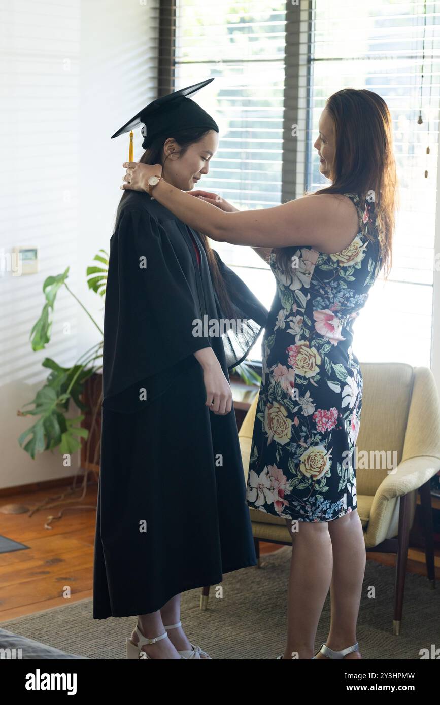 Passt das Abschlusskleid der asiatischen Tochter an, Mutter feiert zu Hause akademische Leistungen Stockfoto