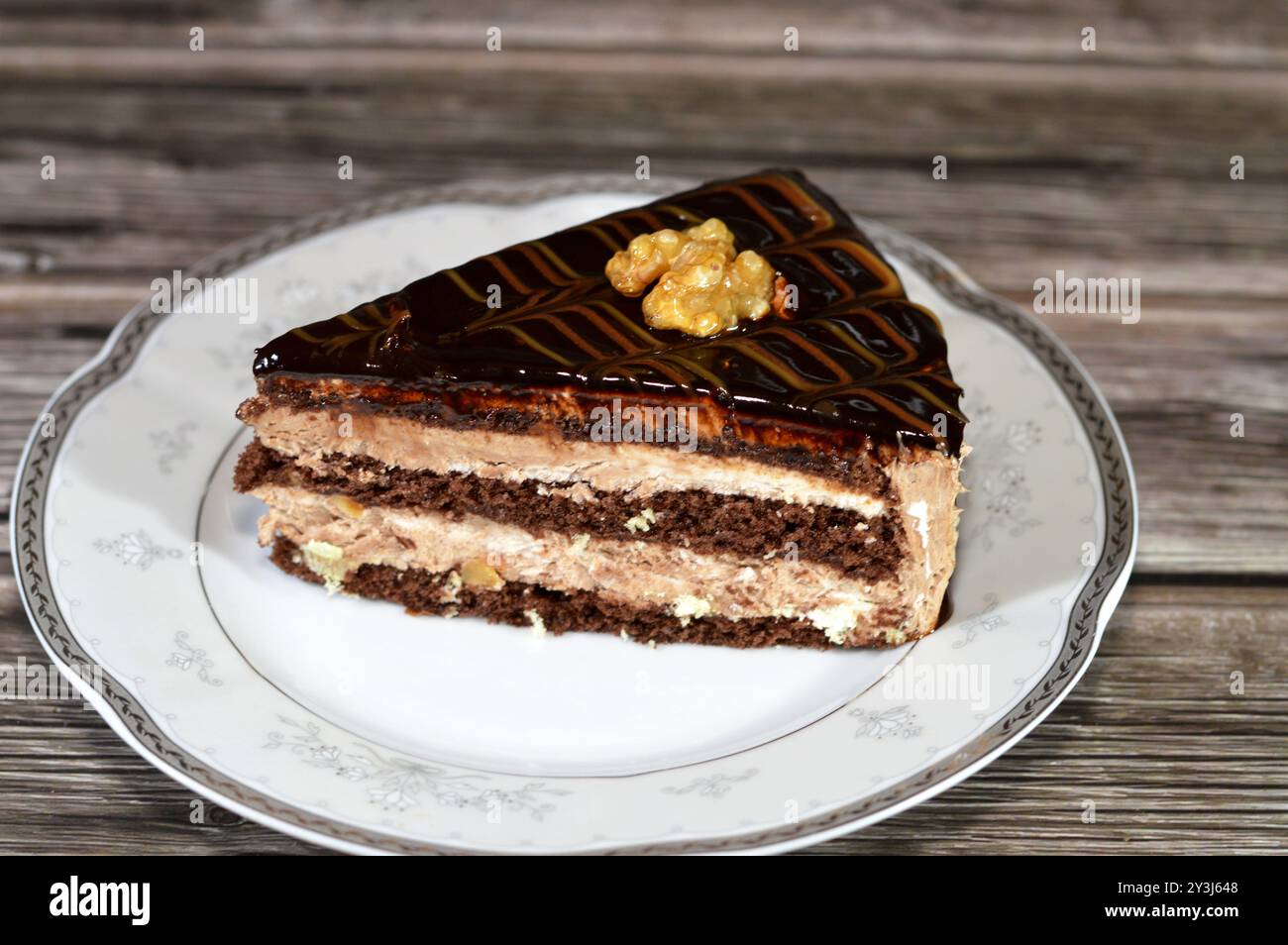 Dreieckiges Schokoladenkuchenstück gefüllt und garniert mit Walnuss, Schichten Schokoladenpaste Creme und Stücken, mit Schichten Schlagsahne, serviert Stockfoto