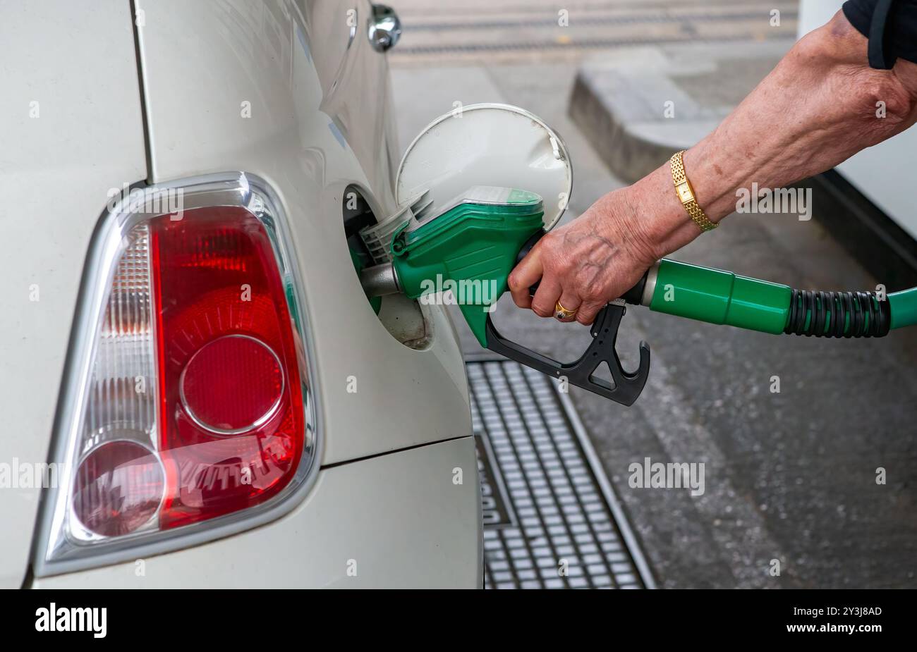 Die Hand einer Frau, die eine grüne Kraftstoffdüse hält, steckt sie in den Benzintank eines weißen Autos und betankt ihr Auto. Stockfoto