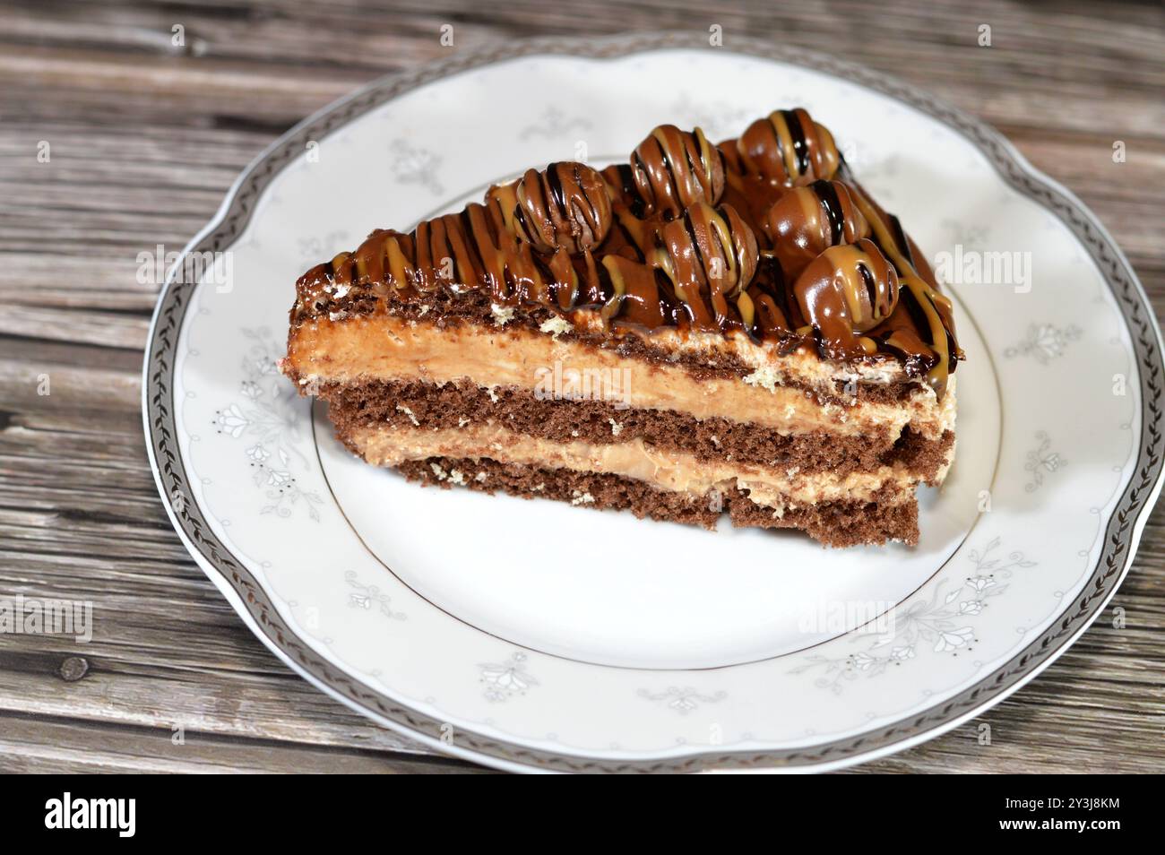 Ein dreieckiges, schwammiges Kuchenstück aus Schokolade, gefüllt mit Schichten Schokoladenpaste Creme und Kugelstücken, mit Kuchenschichten, serviert auf einer Platte Stockfoto