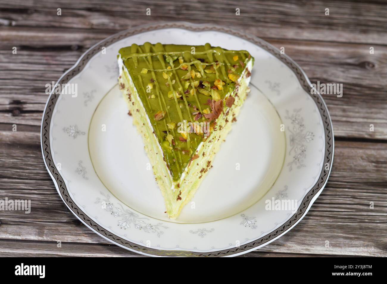 Dreieckiges Stück Pistazienkuchen gefüllt und belegt mit Schichten Pistazienpaste Creme und Stückchen, mit Kuchenschichten, serviert auf einem Teller und ich Stockfoto