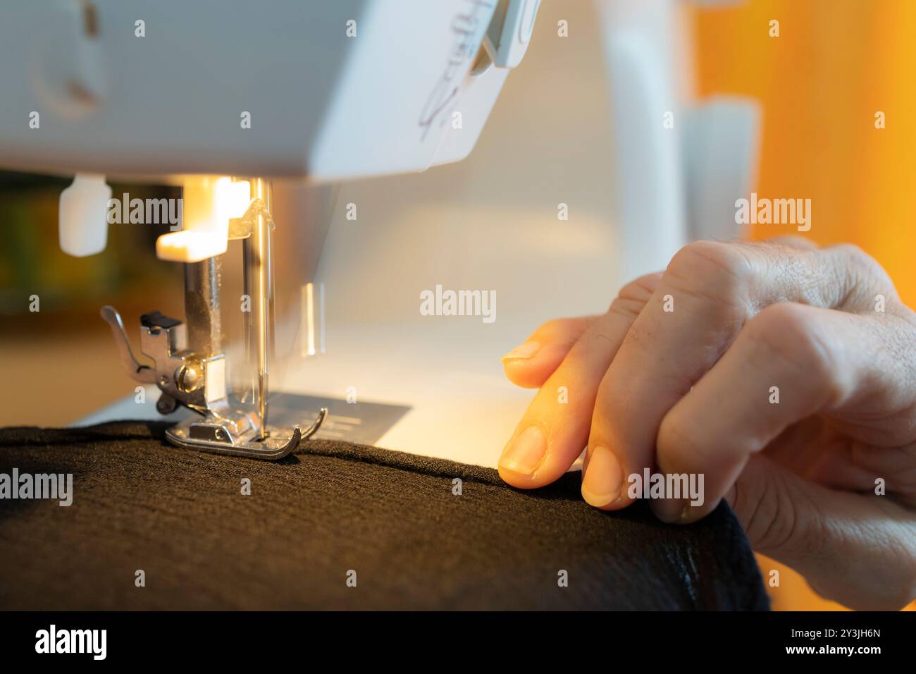 Nahaufnahme der Hände, die den Stoff vorsichtig unter die Nadel einer Nähmaschine führen, um die Handwerkskunst hervorzuheben. Stockfoto