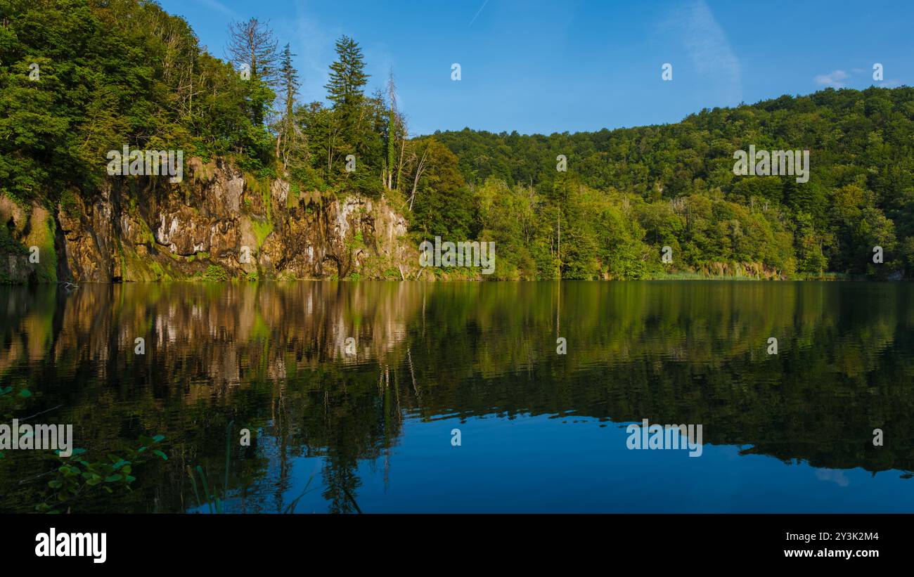 Kristallklares Wasser reflektiert üppiges Grün, während sanfte Wellen über die Plitvicer Seen tanzen. Diese ruhige Umgebung lädt Besucher ein, die Naturwunder zu erkunden, die von strahlendem Sonnenlicht in Kroatien beleuchtet werden Stockfoto