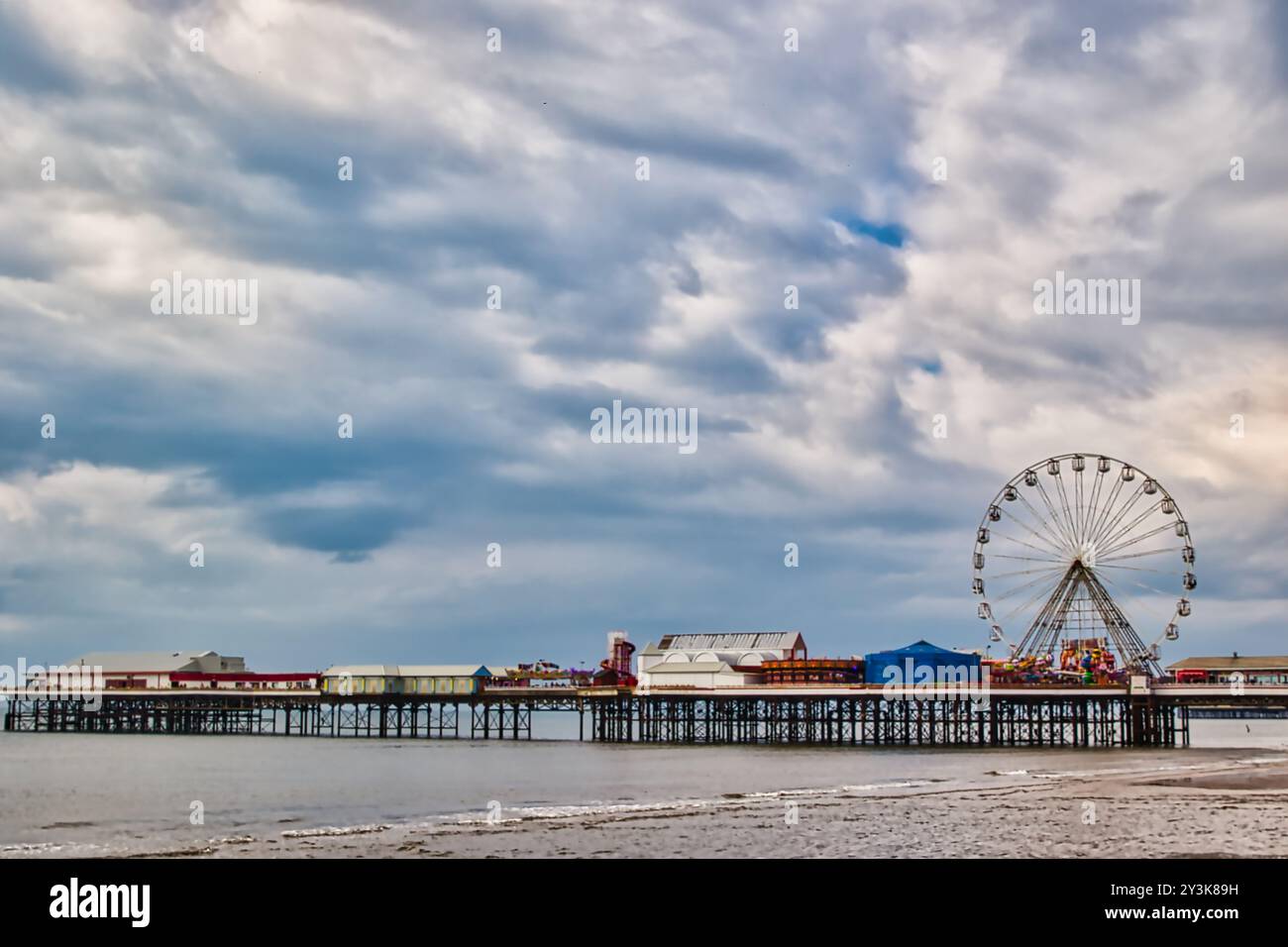 Ein malerischer Blick auf einen Pier mit einem großen Riesenrad vor einem bewölkten Himmel. Das ruhige Wasser reflektiert die Struktur und schafft eine ruhige Atmosphäre. Stockfoto