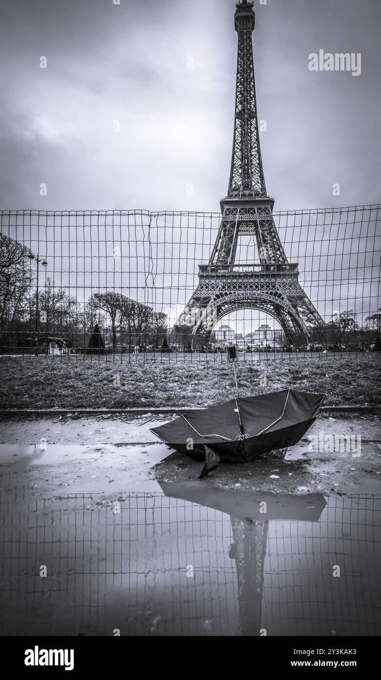 Monochromes Bild mit Eiffelturm an einem regnerischen Tag und einem umgedrehten Regenschirm in einer Pfütze im Vordergrund. Foto aufgenommen in Paris, Frankreich, Europa Stockfoto