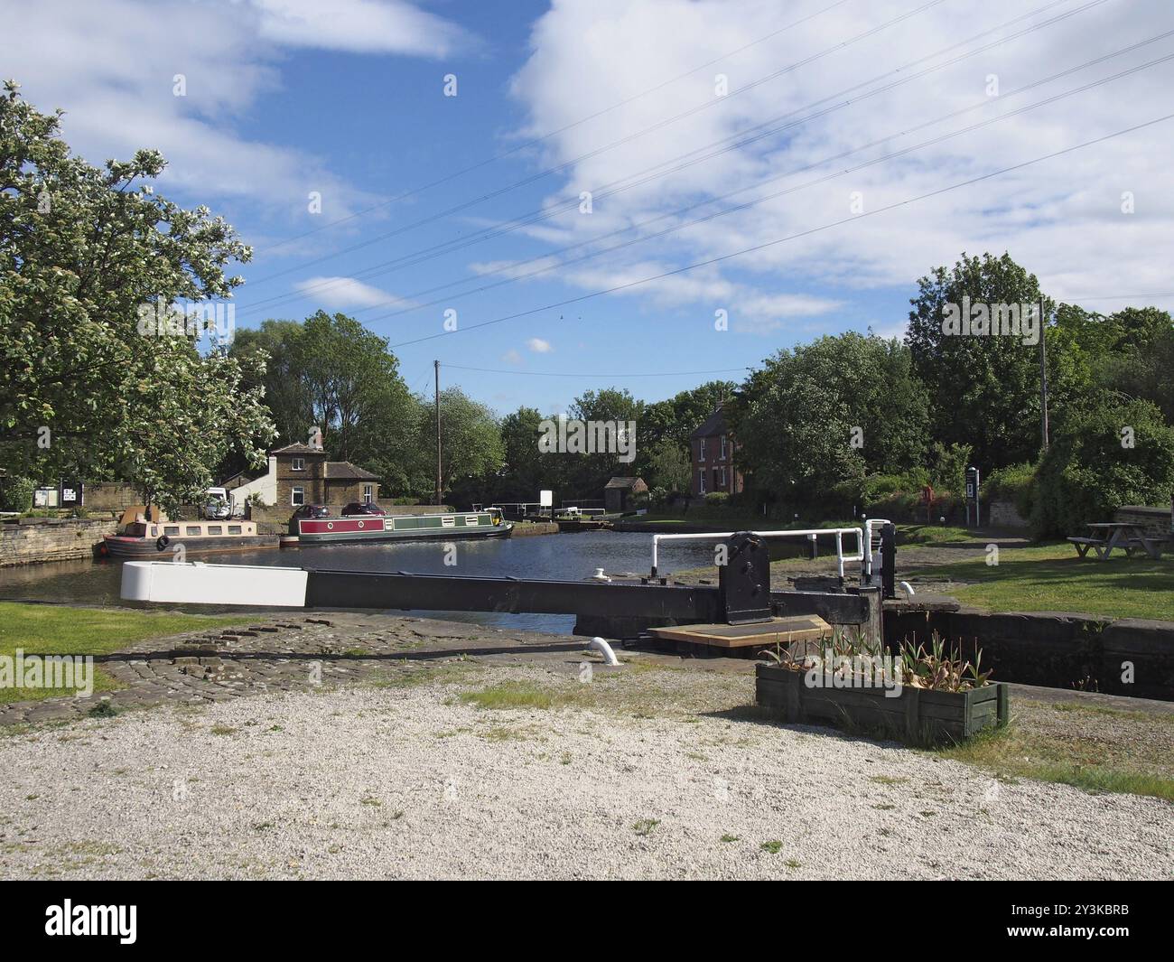 Ein Blick auf die Schleusentore am brighouse Basin am calder und hebble Schifffahrtskanal mit Lastkähnen und Kanalgebäuden, die von Bäumen umgeben sind Stockfoto