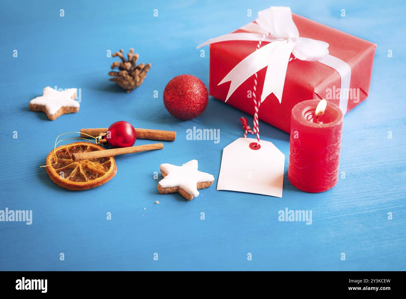 Geschenk verpackt in rotem Papier und mit weißem Band und Bogen gebunden, mit einem leeren Etikett befestigt ist, durch die sternförmige Cookies, Gewürze, Globen umgeben, ein Stockfoto