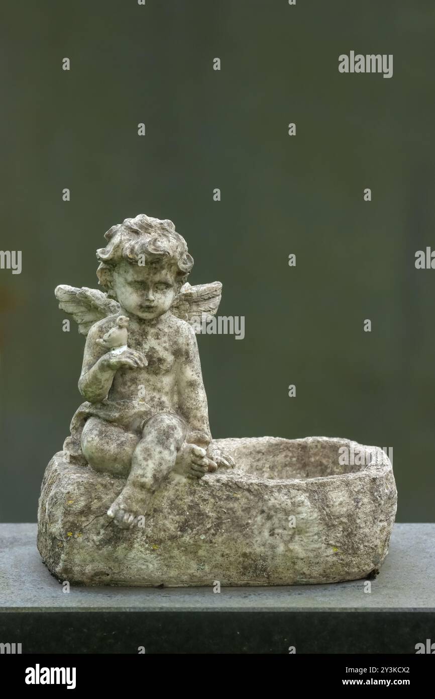 Eine kleine Engelsstatue als Grabdekoration auf einem Friedhof. Das Bild hat einen leeren Platz für Text. Die Statue hat einen grünen Hintergrund im Sommer. Stockfoto