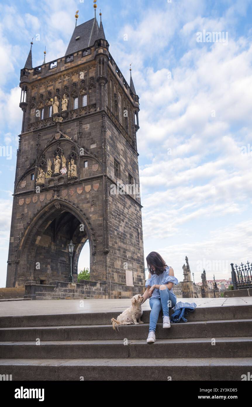 Junge Brünette, die ihren Hund auf der Treppe vor dem Turm auf der Karlsbrücke in der Altstadt von Prag in der Tschechischen Republik streichelt Stockfoto