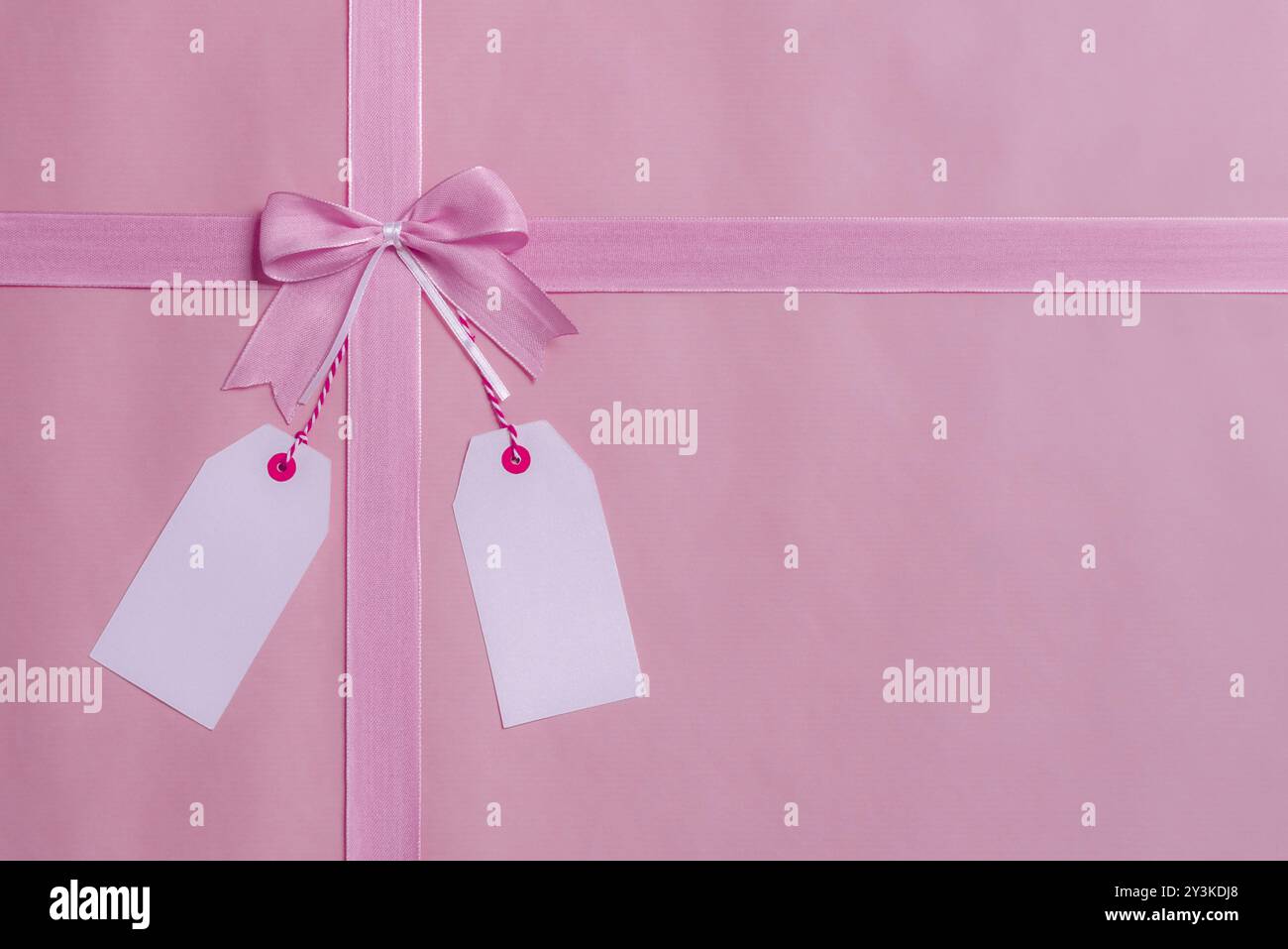 Oberhalb eines Geschenkrahmens mit rosafarbener Schleife und Schleife und zwei leeren Etiketten, die an der Schleife hängen. Grußkarten-Konzept Stockfoto