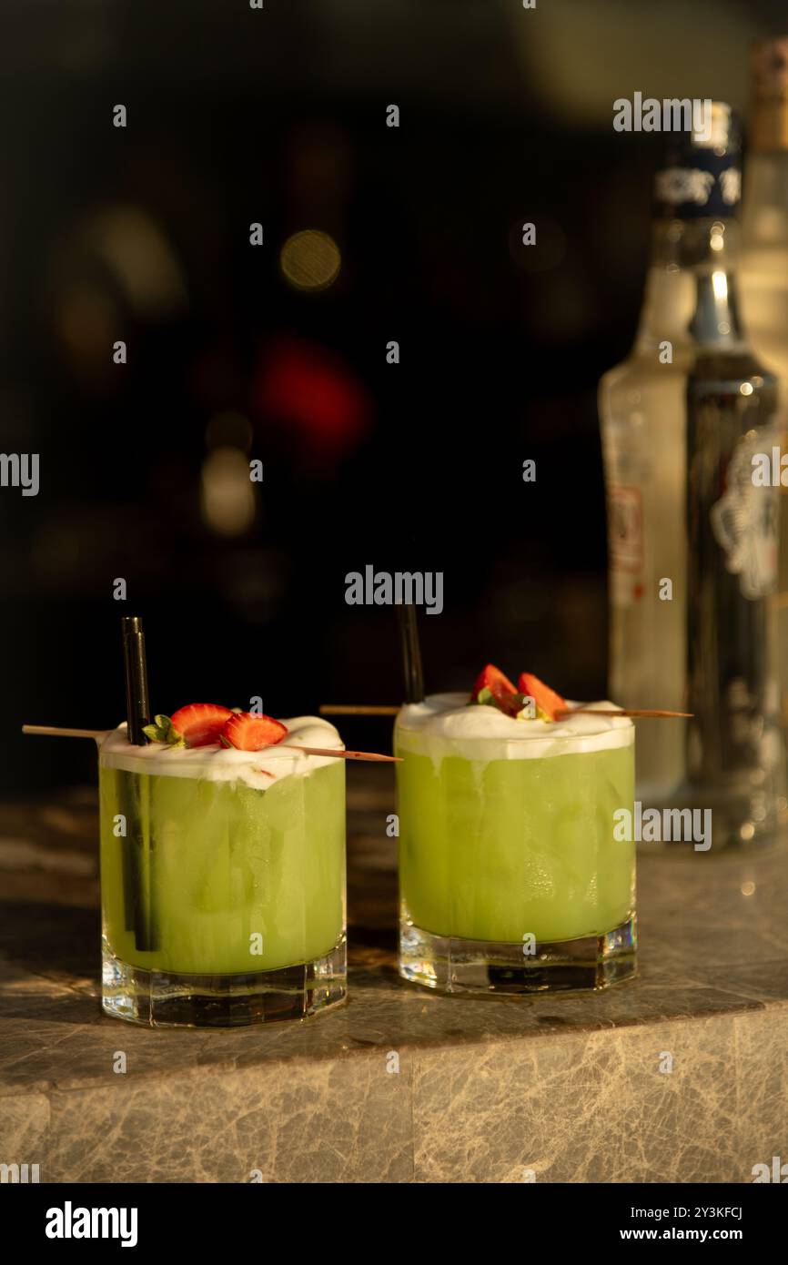 Zwei leuchtend grüne Cocktails, garniert mit Erdbeeren und Schaum auf einer Marmorbar, sorgen für eine perfekte Abendstimmung Stockfoto