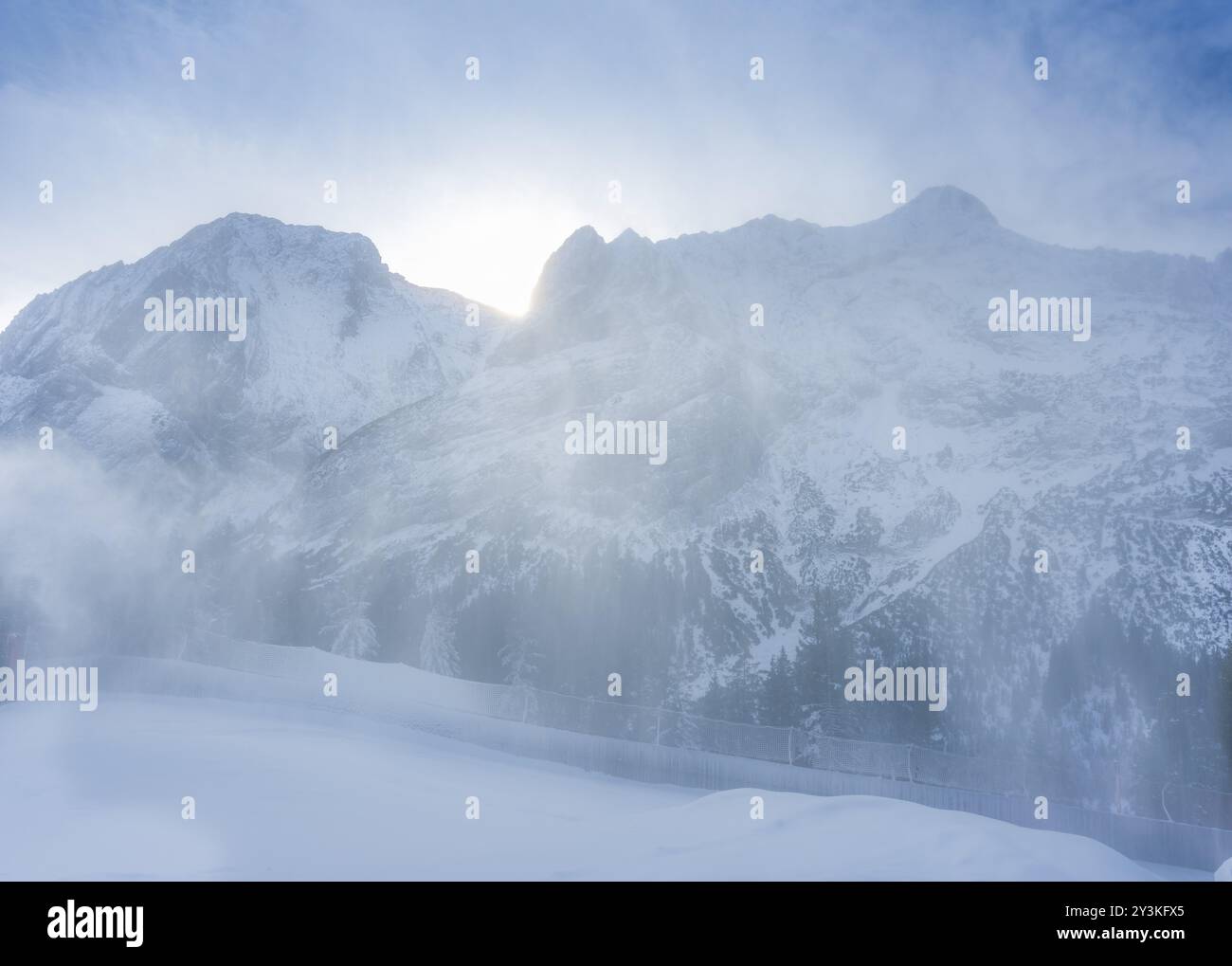 Winterlandschaft mit einem sanften Schneesturm, der den frischen Schnee über die österreichischen Alpen bläst, während die Sonne über den Gipfeln aufgeht Stockfoto