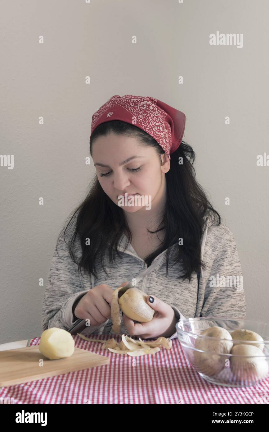 Junge brünette Frau, die Kartoffeln auf einem Tisch im Sonnenlicht schält Stockfoto