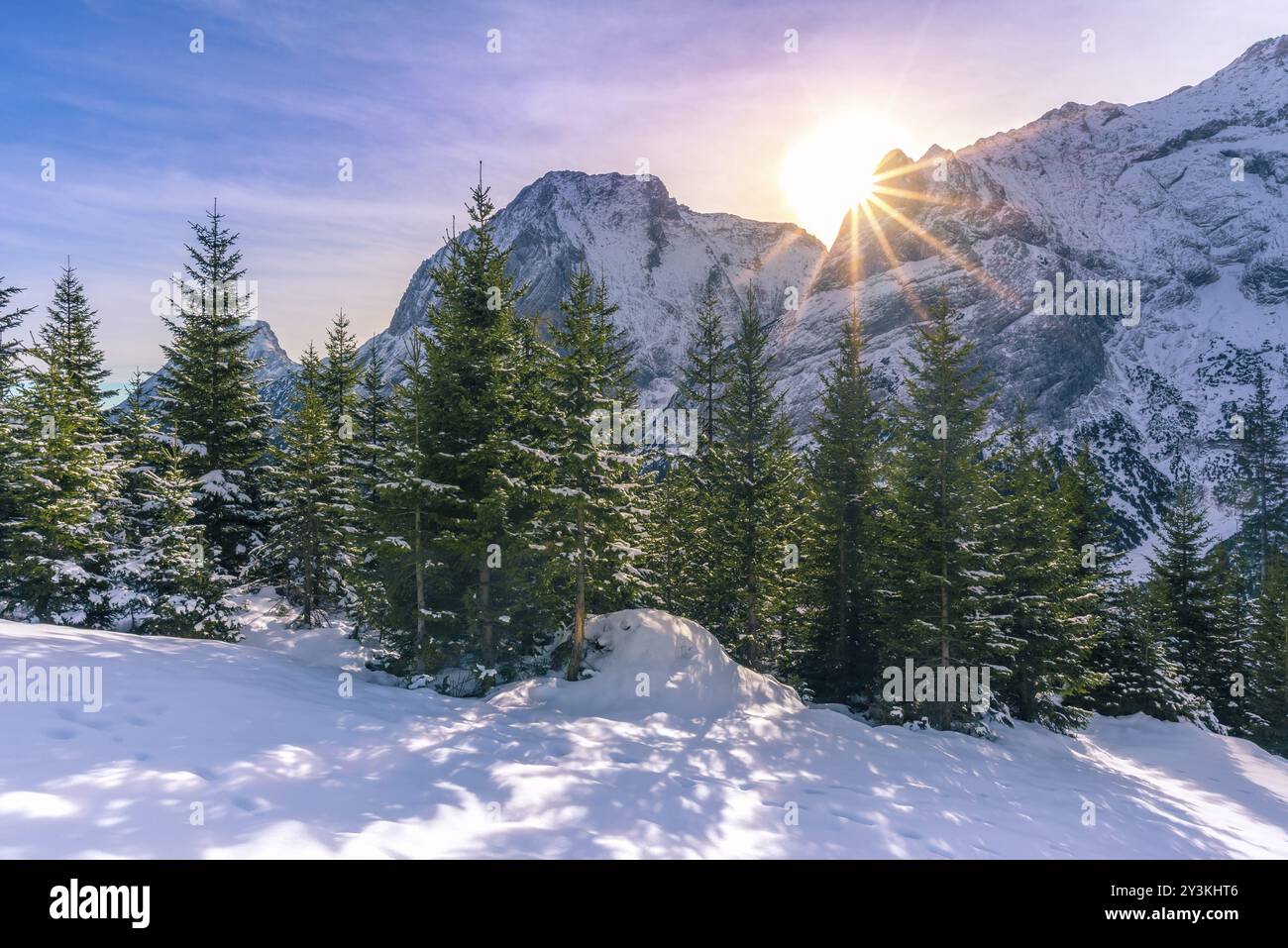 Ruhige Winterlandschaft mit strahlender Sonne über den Gipfeln der österreichischen Alpen und ihren ewig grünen Tannenwäldern Stockfoto