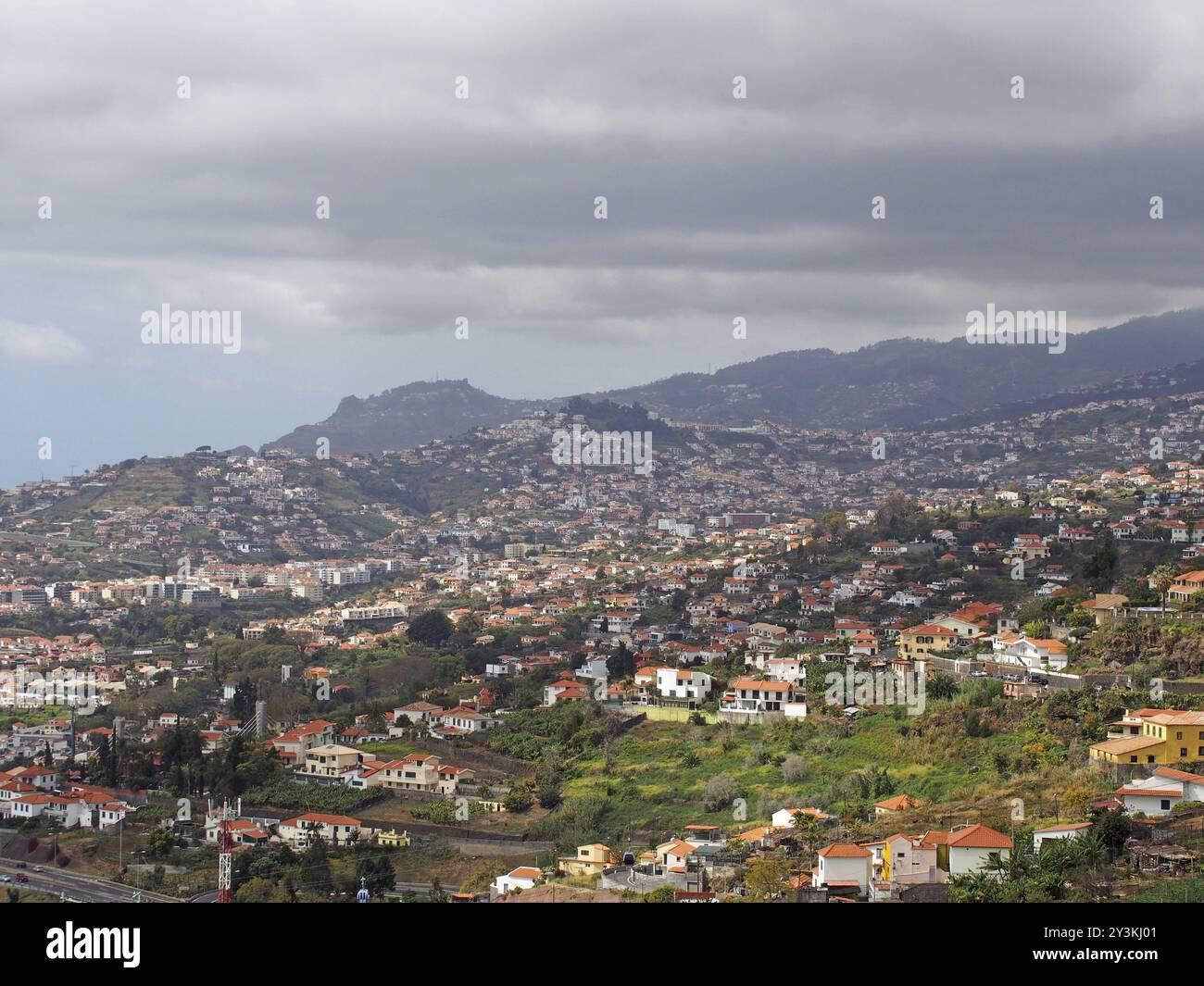 Blick aus der Vogelperspektive auf den Stadtrand von funchal auf Madeira mit Bauernhöfen und Häusern mit Bergen und bewölktem Himmel in der Ferne Stockfoto