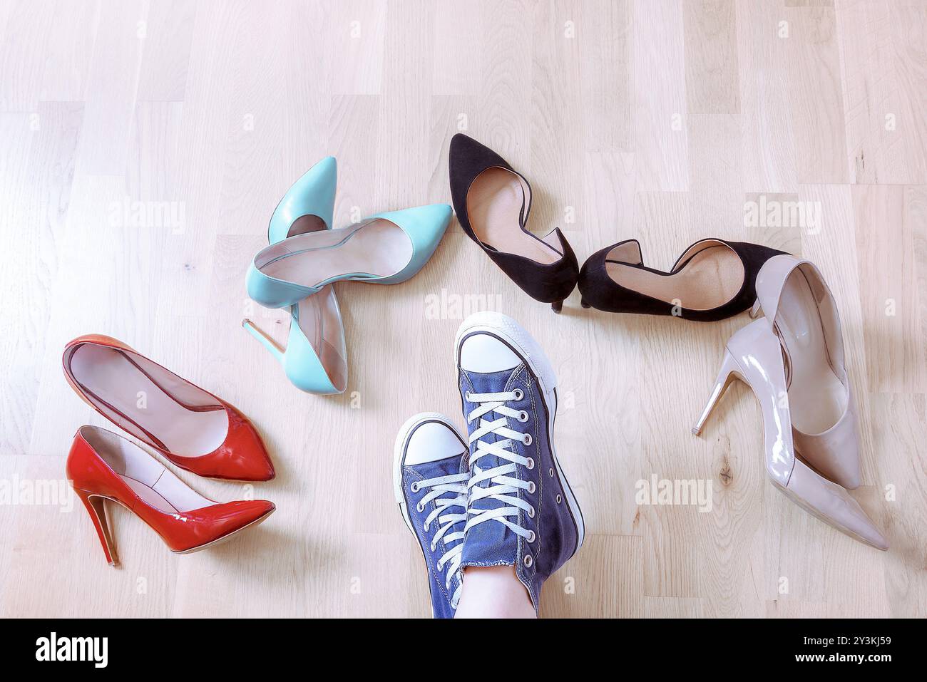 Konzeptionelles Bild mit den Füßen eines Mädchens in Turnschuhen, umgeben von eleganten High-Heels-Schuhen. Entscheiden Sie sich für Komfort und Eleganz Stockfoto