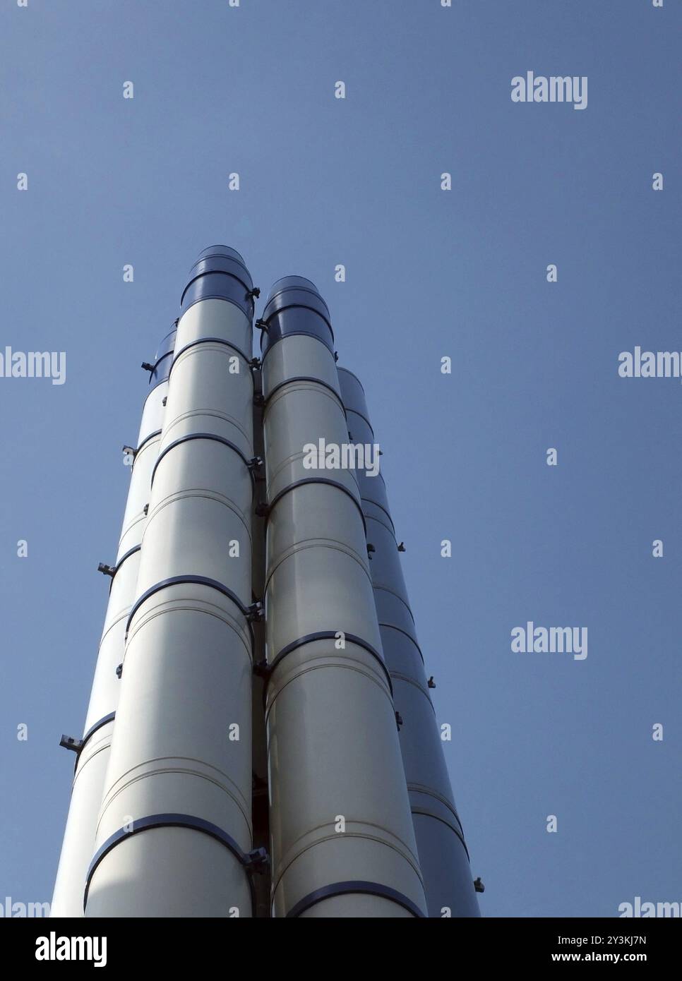 Eine Gruppe von hohen modernen industriellen Stahlschornsteinen, die vor einem hellblauen Himmel und weißen Wolken stehen Stockfoto