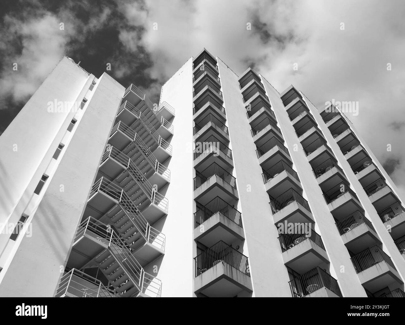 Monochromer, abgewinkelter Detailblick auf ein altes weißes Betonwohnhaus aus den 1960er Jahren mit Stufen und Balkonen gegen Himmel und Wolken Stockfoto