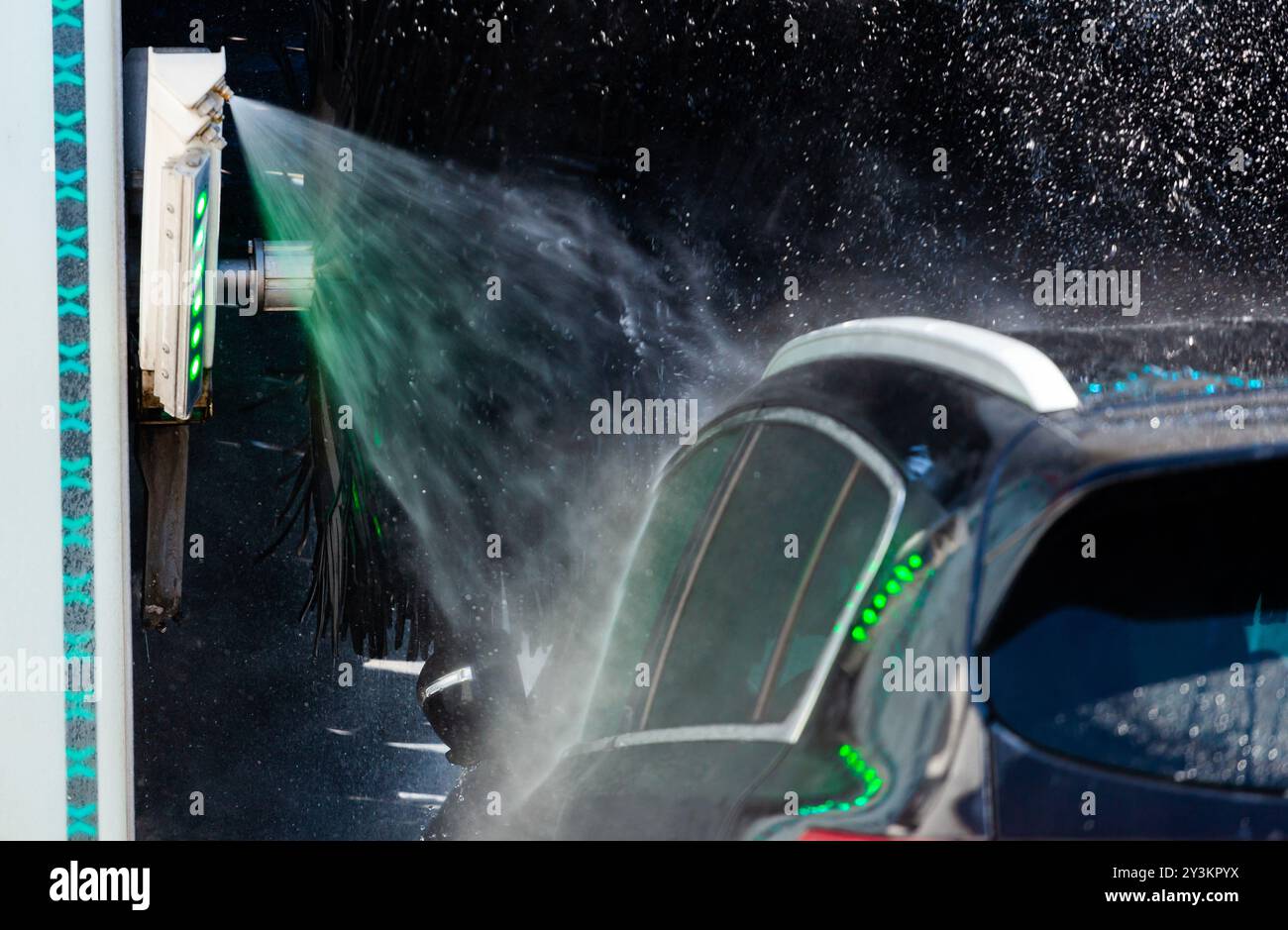 Während des Reinigungsprozesses wird Wasser aus einer automatischen Waschanlage auf ein Fahrzeug gesprüht Stockfoto