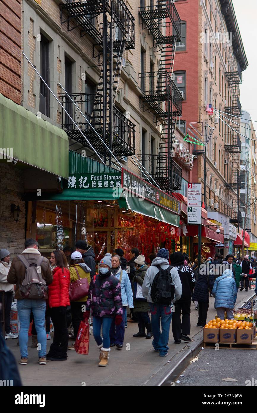 New York, USA – 14. September 2024: Geschäftige Straße mit Menschen, die zwischen Geschäften mit chinesischen Schildern und typischen New Yorker Feuerflüchten spazieren gehen. Stockfoto