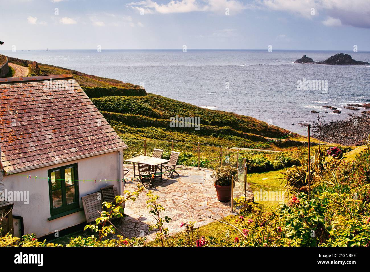 Eine malerische Küstenszene mit einem malerischen Cottage mit einer Steinterrasse mit Blick auf das Meer. Üppige grüne Hügel umgeben die Gegend, und der Himmel ist PA Stockfoto