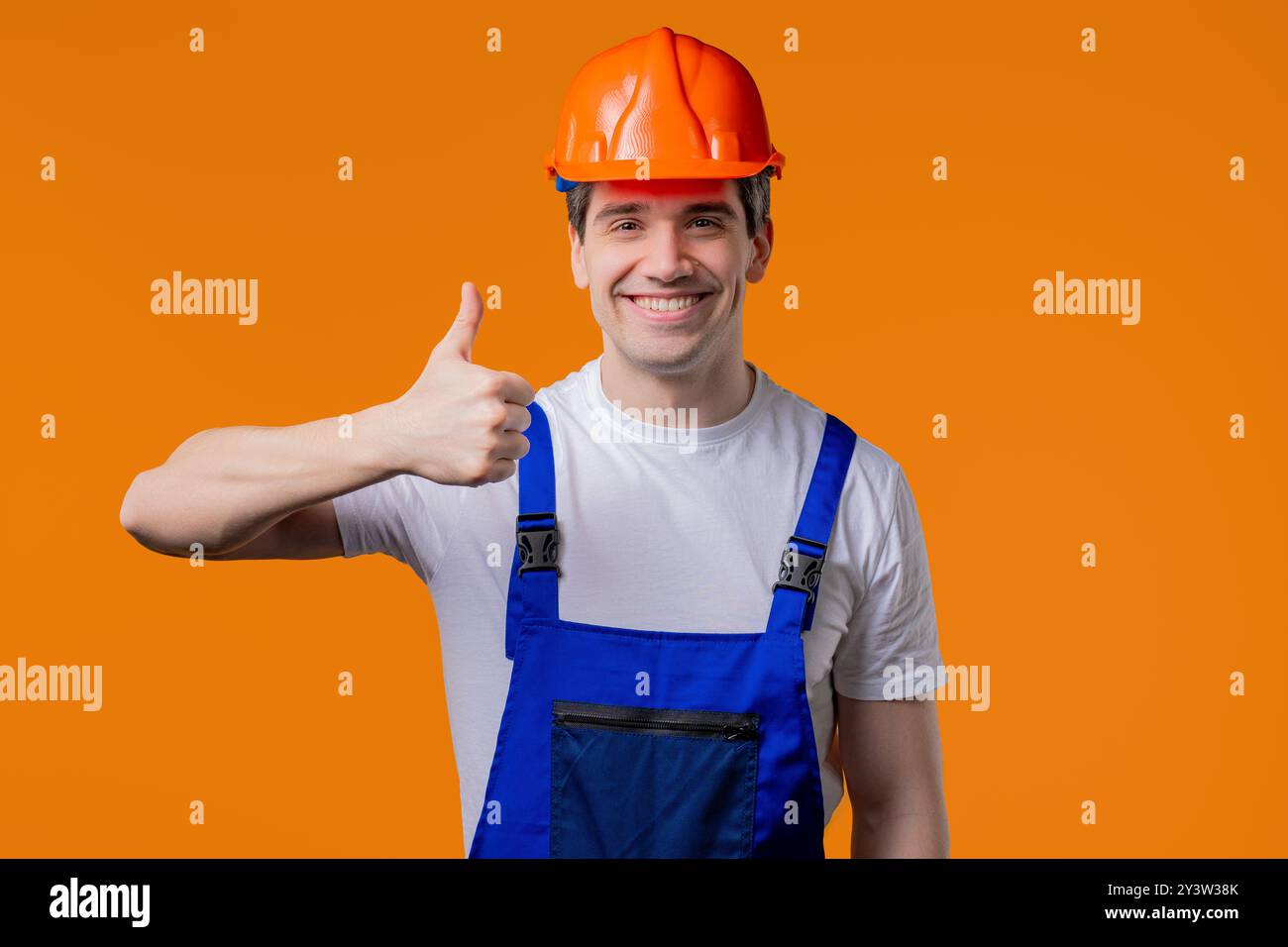 Positiver Baumeister im Helm, Schutzuniform macht Handzeichen wie Daumen hoch Stockfoto
