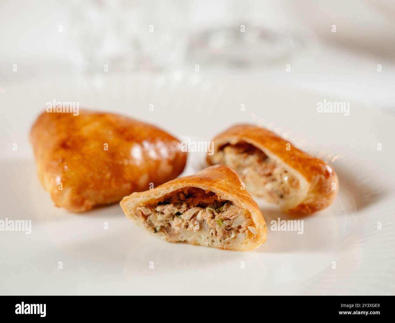 Kleine russische Torten mit gehacktem Thunfisch russischer Piroschki. Gekochter Thunfisch, handportionierte Torten oder Empanadas, die in zwei Hälften geschnitten werden, auf weißem Teller im eleganten Restaurant. Selektiver Fokus, Nahaufnahme. Stockfoto