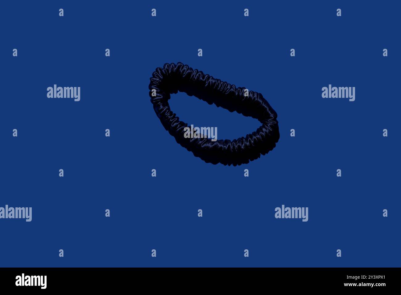 Seidenhaar-Scrunchie für Mädchen und Frauen auf einem ruhigen blauen Hintergrund ist perfekt für die Werbung für Haaraccessoires, Schönheitsprodukte oder Modetrends. Verwenden Stockfoto